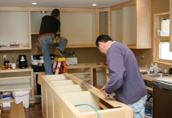 Close-up of kitchen cabinet installation process showing craftsman measuring wood for island in remodeled Thousand Oaks kitchen.